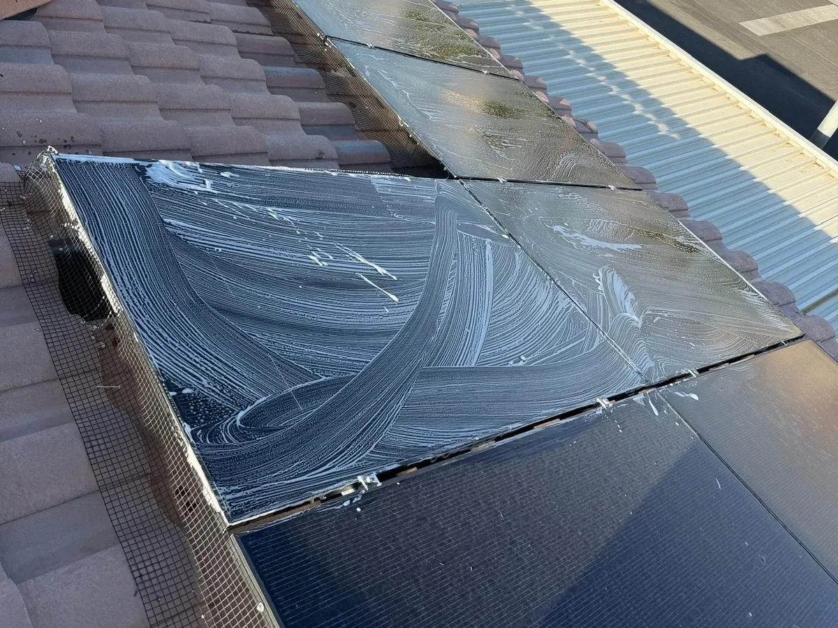 Close-up of a solar panel being washed by hand, suds still on the glass